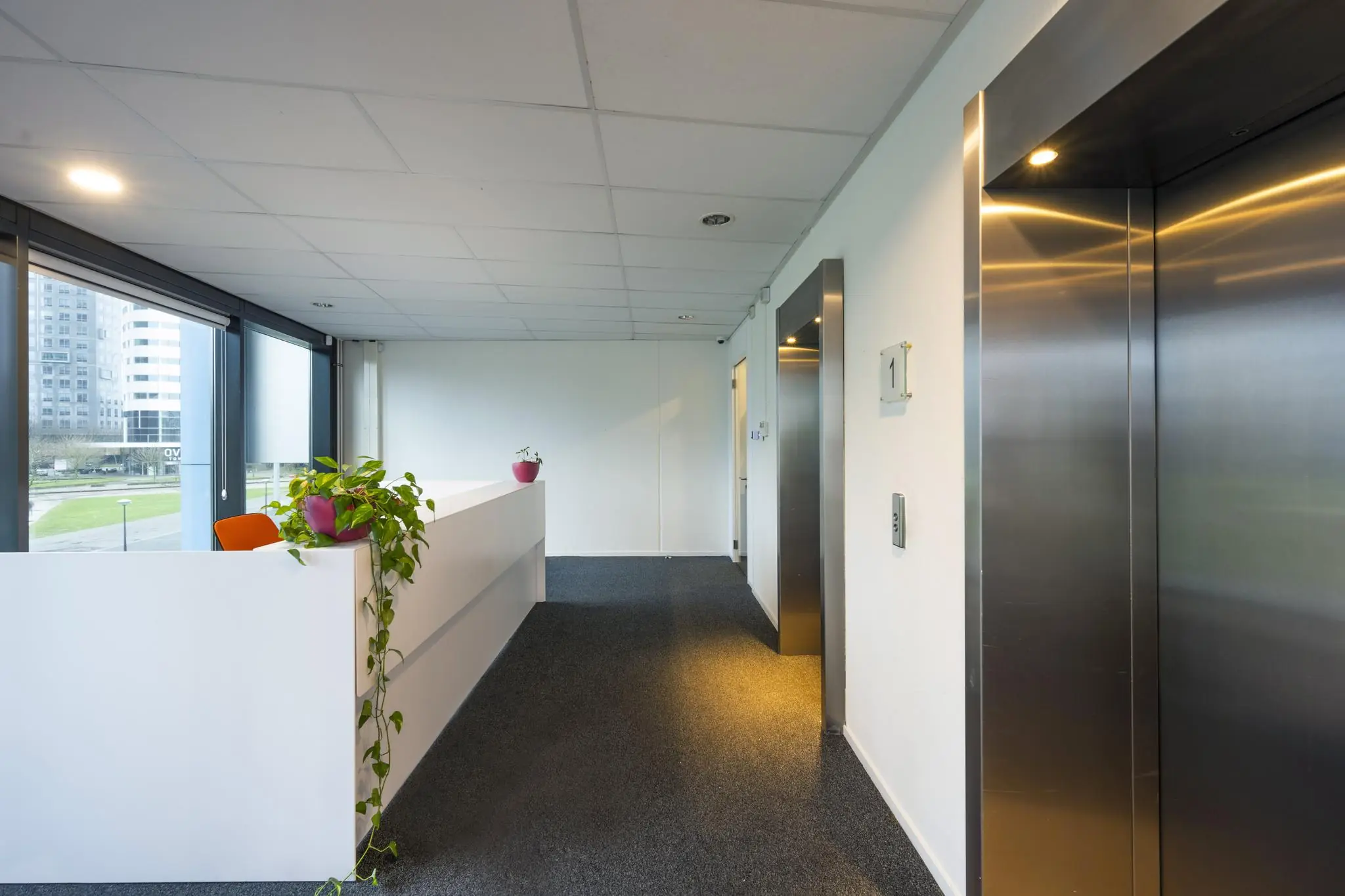 Moderne kantoorruimte met ontvangstbalie, planten en liften aan de Johan Cruijff Boulevard.